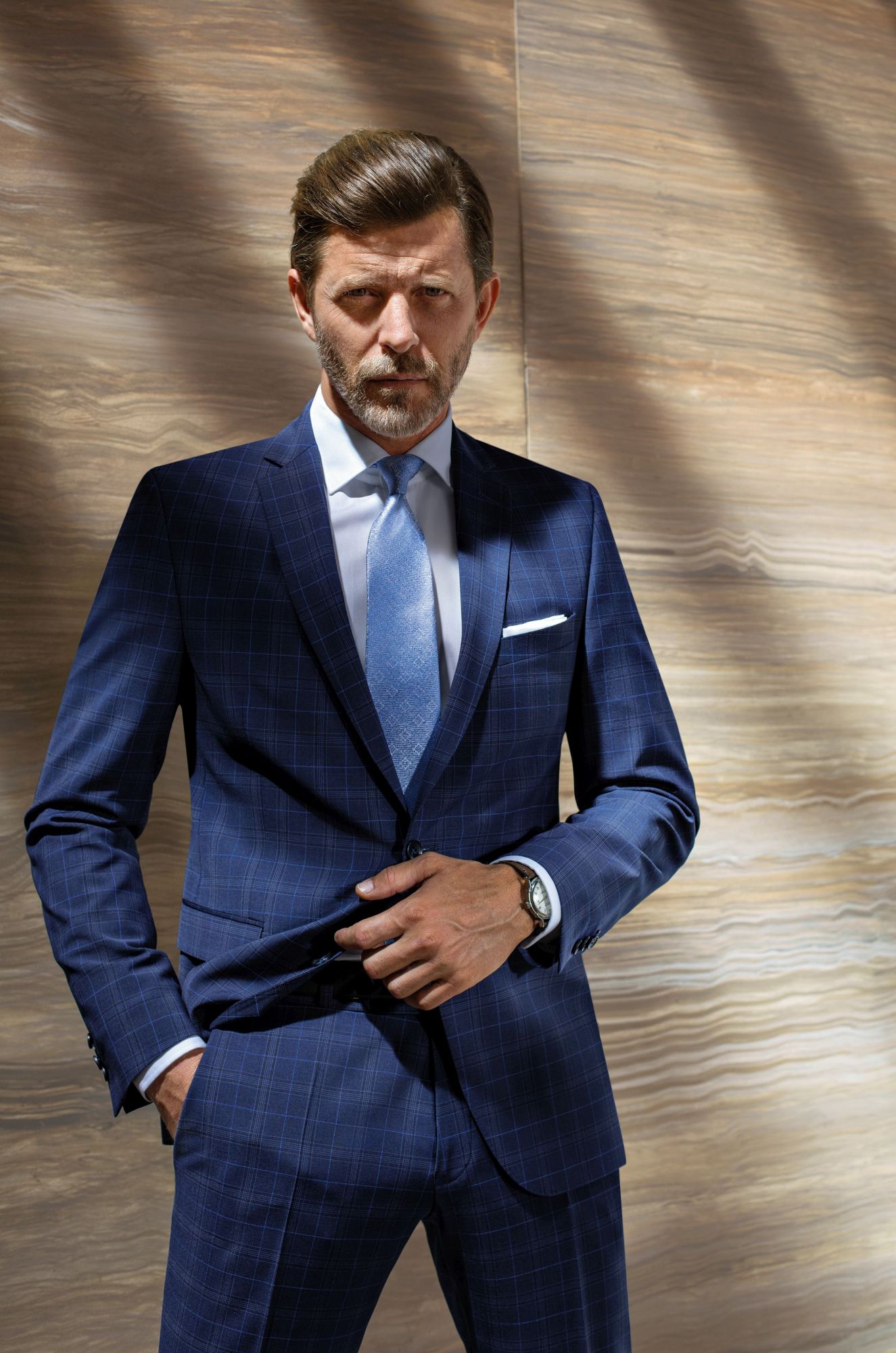 mężczyzna w niebieskim garniturze biznesowym w kratę, w niebieskim krawacie, w białej koszuli.